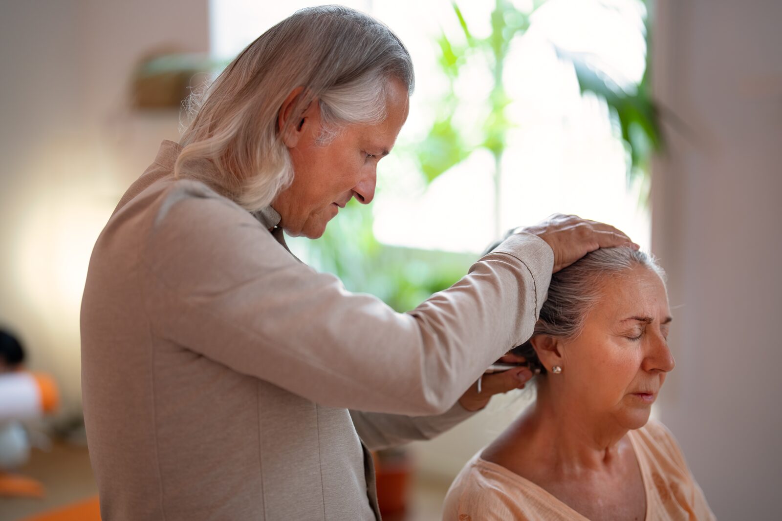 Neck-related headache: neck assessment in Málaga José De San Juan Guerrero, D.C., assessing the neck of a seated patient, one hand on her head and one at the base of her skull, in his Málaga clinic